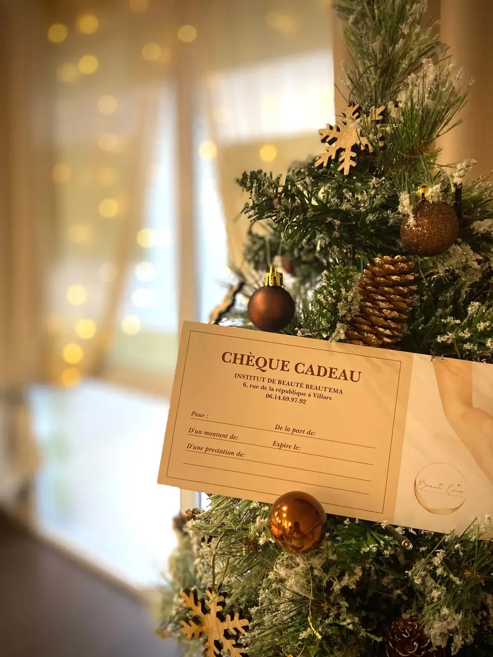 Un chèque cadeau Beaut’Ema glissé dans un sapin décoré
